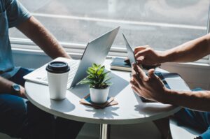 Two persons with laptops in conversation at a table